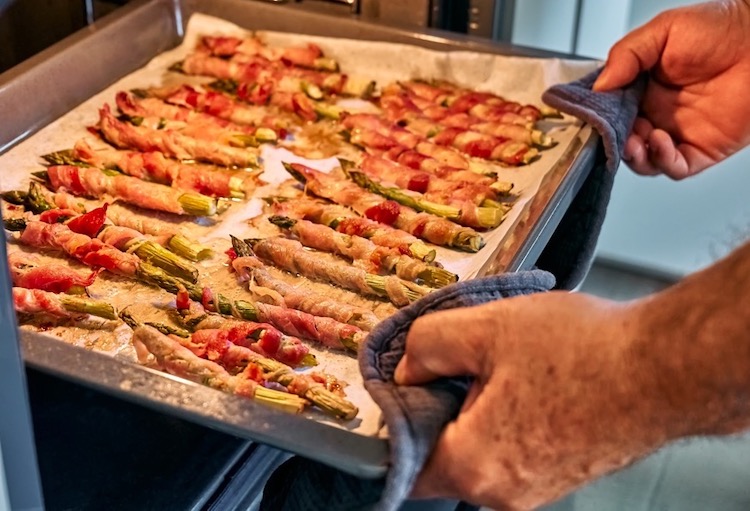 Pulling bacon wrapped asparagus spears out of the oven. 