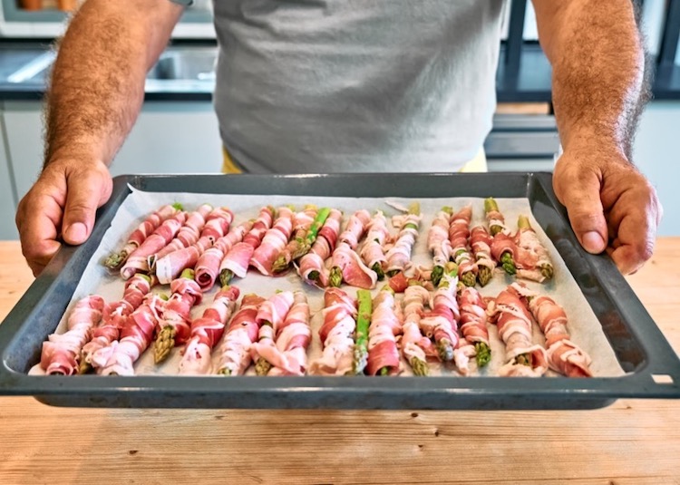 A sheet pan full of asparagus spears wrapped in bacon, ready to be cooked in the oven at 400° F for 20-25 minutes or until tender with crispy bacon. 