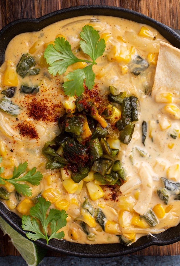A delicious close up view of a cheesy dip in a cast iron skillet made with corn, poblanos, cream cheese, sour cream, cheddar cheese and spices. Serve at your next party with tortilla chips for dipping. 